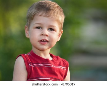A smiling little boy is standing outdoors