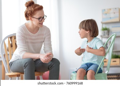 Smiling little boy talking with cheerful child psychotherapist during therapy session at office