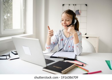 Smiling Little Caucasian Girl In Headphones Handwrite Study Online Using Laptop At Home, Cute Happy Small Child In Earphones Take Internet Web Lesson Or Class On Computer, Homeschooling Concept