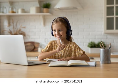 Smiling little Caucasian girl in headphones looking at laptop screen studying online at home, interested cute kid watching webinar listening to lecture, taking notes, homeschooling concept - Powered by Shutterstock