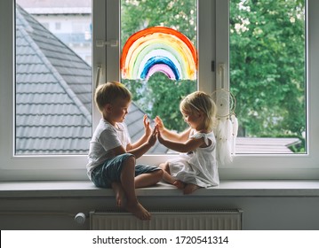 Smiling Little Children On Background Of Painting Rainbow On Window. Photo Of Kids Leisure At Home, Childcare, Safety Joy Symbol, Family Life. Child Art And Creative.