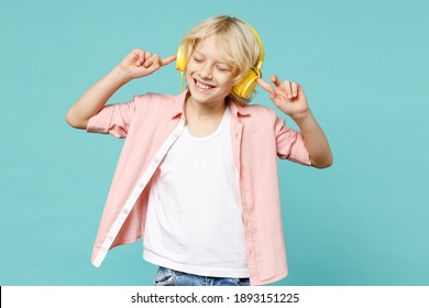 Smiling little curly kid boy 10s years old wearing casual pink shirt listening music with headphones isolated on blue turquoise color background children studio portrait. Childhood lifestyle concept - Powered by Shutterstock