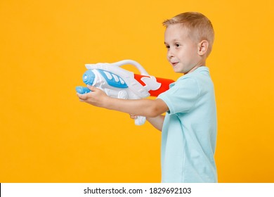 Smiling Little Fun Male Fair-haired Brown-eyed Kid Boy 5-6 Years Old Wearing Stylish Blue Turquoise T-shirt Polo Hold In Hand Toy Water Gun Isolated On Yellow Color Background, Child Studio Portrait