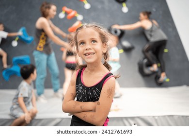 Smiling little girl climber standing arms crossed in sports center. Female child looking up during rock climbing class. Essence of pursuing hobbies. - Powered by Shutterstock