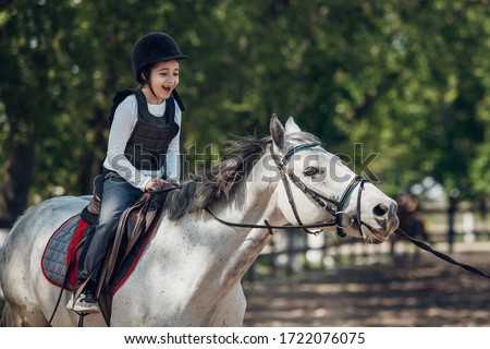 Smiling Little Girl in helmet Learning Horseback Riding. Instructor teaches kid Equestrian.