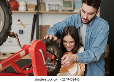 Smiling little girl helping father repair her bicycle while holding part of wheel and using wrench to fix it in garage with household supplies - Powered by Shutterstock