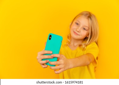 Smiling little girl kid showing blue screen of new popular mobile phone on light yellow background.