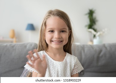 Smiling Little Girl Looking At Camera, Waving Hand, Greeting, Making Video Call To Relatives, Recording Vlog For Channel, Head Shot Portrait Of Cute Child, Sitting On Cozy Sofa At Home