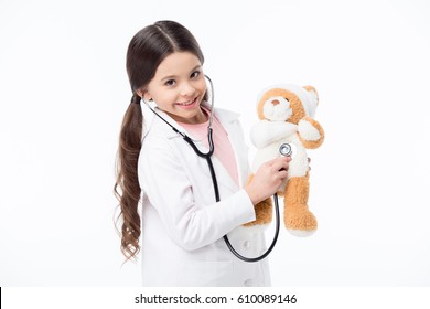 Smiling little girl playing doctor and listening teddy bear with stethoscope isolated on white - Powered by Shutterstock