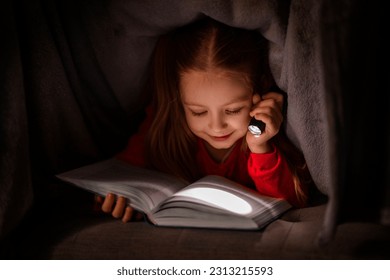 Smiling Little Girl Reading Book While Hiding Under Blanket With Flashlight, Cheerful Cute Female Child Holding Pocket Torch In The Dark And Enjoying Her Favorite Faily Tailes, Closeup Shot