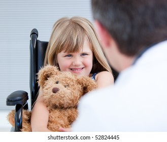 Smiling Little Girl Sitting On The Wheelchair With Her Teddy Bear At The Hospital