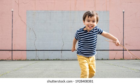 Smiling Little Running Towards Camera On Basque Pelota Court, Toddler Holding Twigs In His Left Hand.