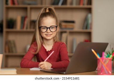 Smiling Little Schoolgirl Posing Near Laptop Computer Taking Notes Sitting Looking At Camera Wearing Eyewear At Home. E-Learning, Education And Internet Concept - Powered by Shutterstock