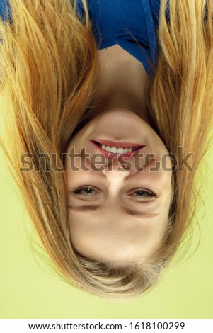 Smiling, looks happy. Inverted portrait of caucasian young woman on yellow studio background. Human emotions are not what they seem when you're looking. Facial expression, funny view, advertisement.