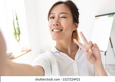 Smiling Lovely Young Asian Businsswoman Taking A Selfie While Standing At The Office, Showing Peace Gesture