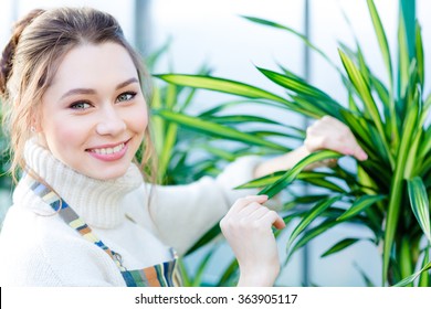 Smiling lovely young woman gardener in uniform working and taking care of ficus in greenhouse - Powered by Shutterstock