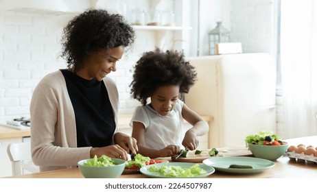 Smiling loving African American mother and little daughter prepare healthy delicious salad in kitchen. Happy caring biracial mom and small ethnic girl child cook together at home. Family concept. - Powered by Shutterstock