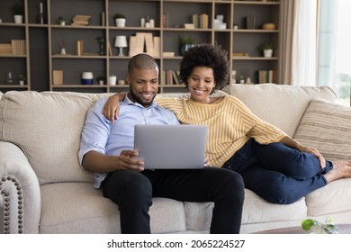 Smiling Loving Bonding Young Mixed Race Family Couple Using Computer, Watching Comedian Movie, Buying Goods In Internet Store, Booking Tickets Or Hotel, Reading News Or Web Surfing Useful Information.