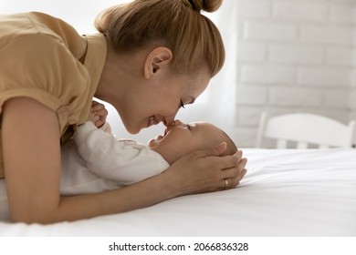 Smiling loving mother and baby touching noses close up, enjoying tender moment, lying on comfortable bed at home, happy young mom with newborn child kid having fun, motherhood and childcare concept