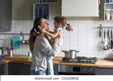 Smiling loving single mother holding cute little child daughter having fun together, happy family of young caring mom and excited kid girl laughing playing at home while cooking in the kitchen