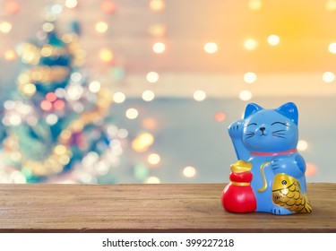 Smiling Lucky Cat Bank On Wooden Plank With Bokeh Christmas Tree Background With Copy Space. Business Concept For Saving Money.