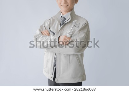 Smiling maintenance worker in uniform standing with arms crossed in a friendly studio portrait.