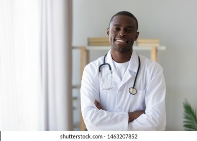 Smiling male african american professional young doctor stand arms crossed wear medical uniform looking at camera, happy confident black man general practitioner with stethoscope in office, portrait