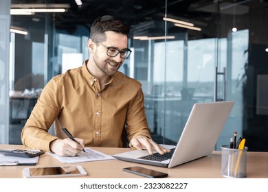 Smiling male businessman sits in the office at the table, works with documents and talks with conducts a business meeting online.