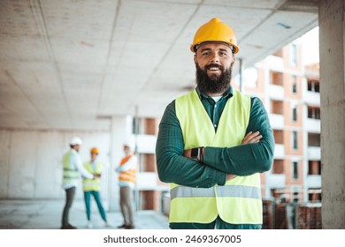 A smiling male construction worker in a yellow hard hat and reflective vest stands with arms crossed at a busy site, with colleagues in the background. - Powered by Shutterstock