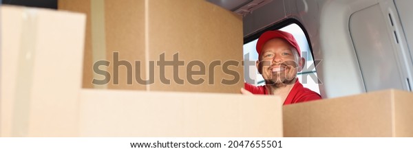 Smiling\
male courier pulls out cardboard box from\
car