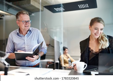 Smiling Male And Female Colleagues Working While Standing At Desk With Glass Shield In Office During Coronavirus