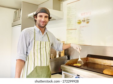 Smiling Male Fry Cook Looking Pleased While Frying A Freshly Made Hamburger Patty In A Takeaway Food Stall Kitchen