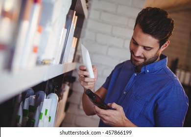 Smiling Male Hair Dresser Selecting Shampoo From Shelf At A Salon