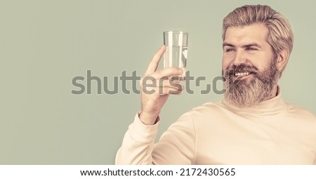 Smiling male holding transparent glass in her hand. Happy beard man drinking water.