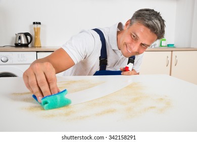 Smiling Male Janitor Cleaning Counter With Sponge At Home