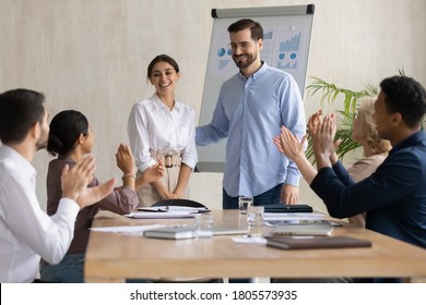 Smiling male leader praising happy millennial arab colleague at group meeting. Smiling diverse coworkers applauding, supporting new worker or congratulating with personal professional achievement.