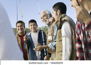 Smiling Male Members Of Three Generation Family Holding Fishing Rods Outdoors