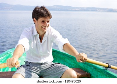 Smiling male model rowing a green boat on a lake