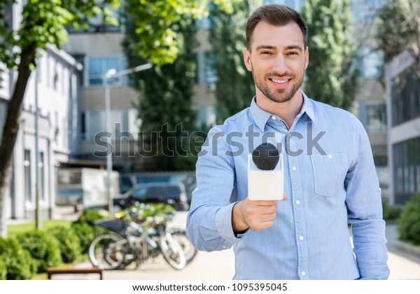 smiling male news reporter taking interview with\
microphone   