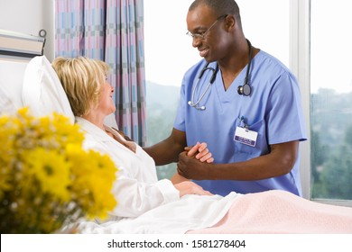 Smiling Male Nurse Holding Hands With Female Patient In Hospital Bed