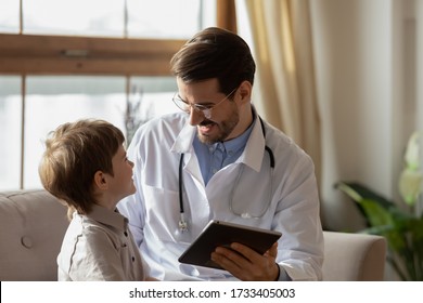 Smiling male pediatrician with little boy patient talk using tablet at consultation in hospital, caring doctor or GP do checkup speak with small child at clinic meeting, medicine, healthcare concept