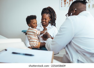 Smiling male pediatrician in white medical uniform holding clipboard, listening to young mother with kid son at checkup meeting, professional children doctor consultation, healthcare concept. - Powered by Shutterstock