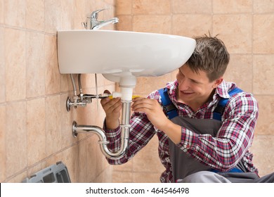 Smiling Male Plumber Repairing Sink In Bathroom