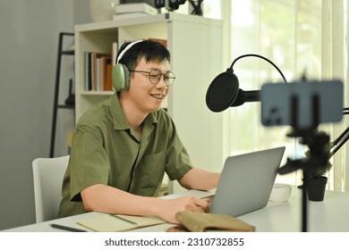 Smiling male podcaster wearing headphone streaming and broadcasting podcast from home studio - Shutterstock ID 2310732855