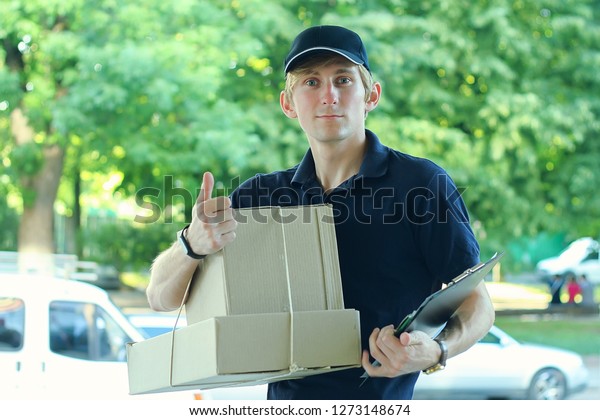 Smiling male postal delivery courier\
man outdoors in front of cargo van delivering\
package
