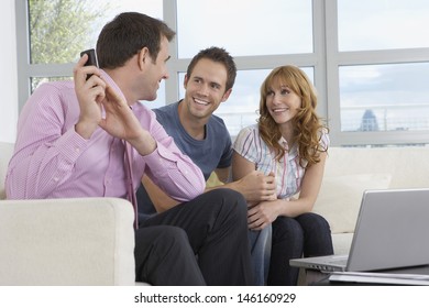 Smiling Male Real Estate Agent Using Mobile Phone By Couple In New Home