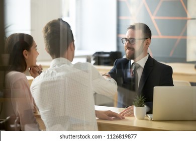 Smiling male realtor or broker shaking hand of excited buyers couple, negotiating about first house purchase or taking loan, insurance agent welcoming clients with handshake at consultation meeting