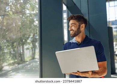 Smiling male sales manager working on laptop standing in office during working day and looks away - Powered by Shutterstock