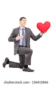 A smiling male in a suit kneeling with red heart isolated on white background