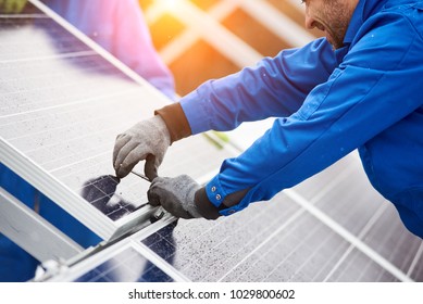Smiling male technician in blue suit installing photovoltaic blue solar modules with screw. Man electrician panel sun sustainable resources renewable energy source alternative innovation